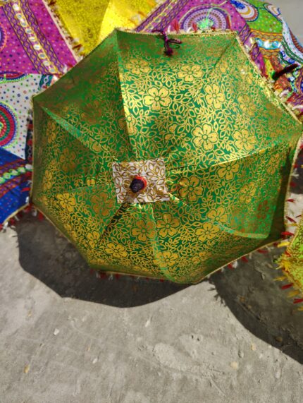 Green and gold patterned umbrella on sand.