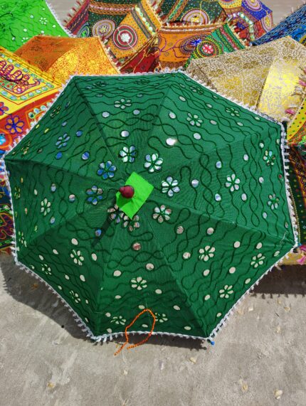 Green umbrella with mirror embellishments on sand.