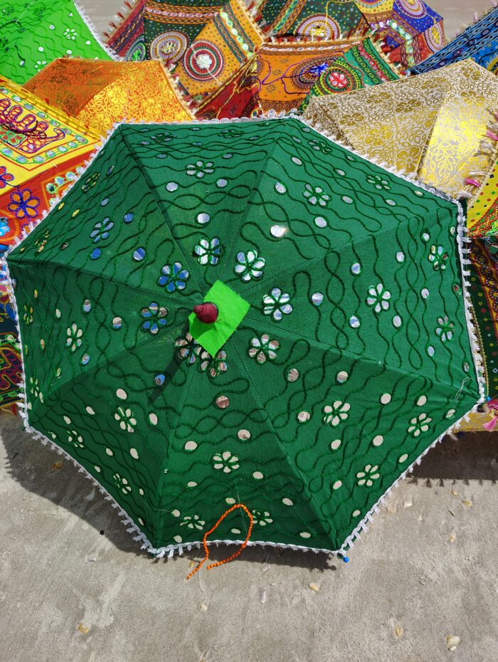 Green umbrella with mirror embellishments on sand.