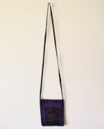 Purple fabric crossbody bag on white wall.