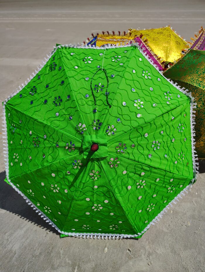 Green embroidered umbrella on sand.