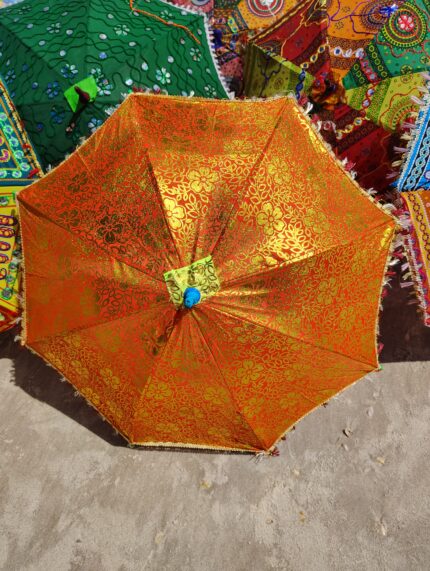 Orange and gold patterned umbrella on sand.